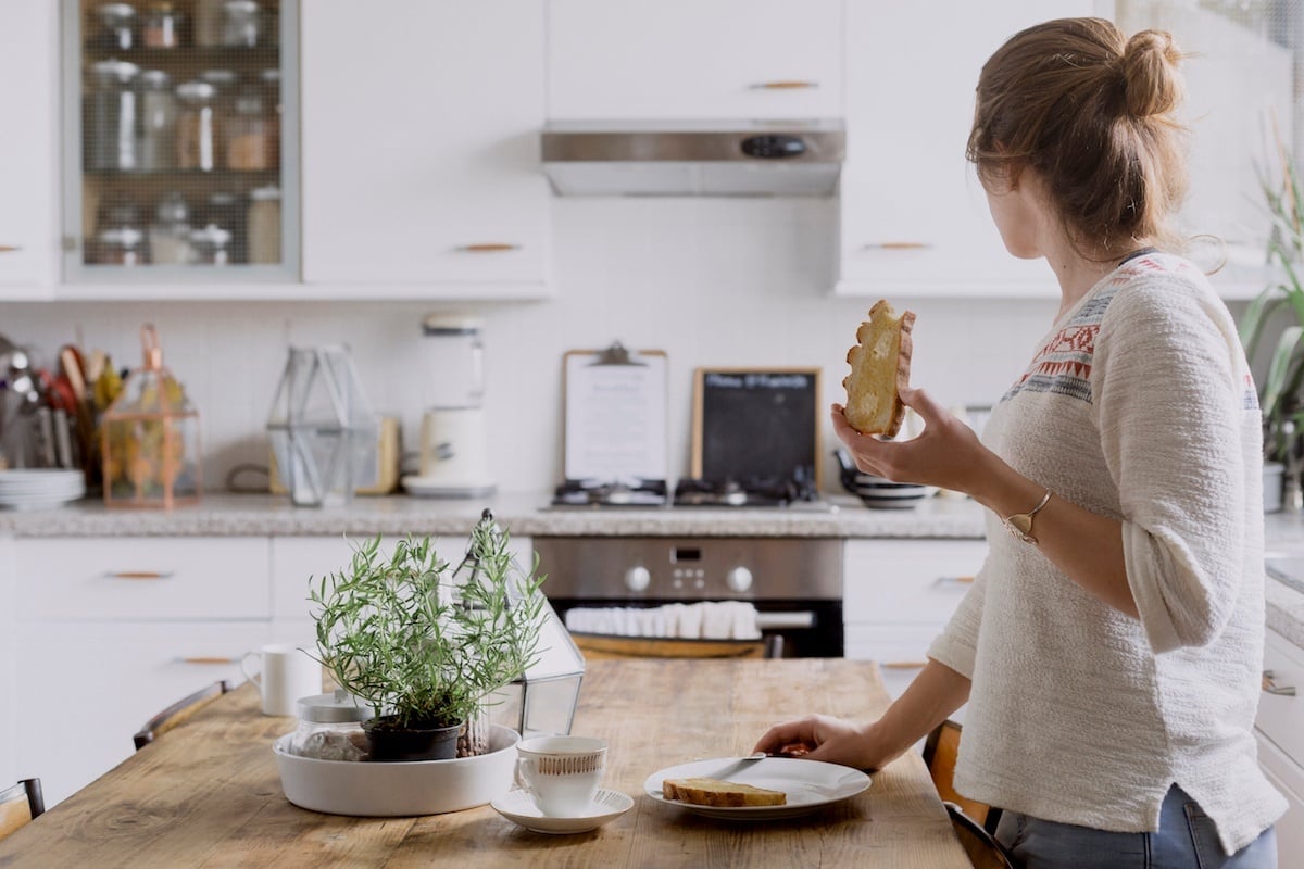 Frau steht in Küche an der Arbeitsfläche und ist ein Brot